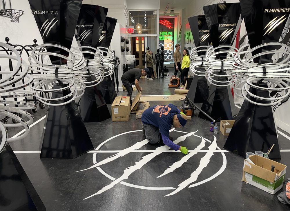 Kwazi installing a white claw-mark graphic into a black wood floor in a retail store