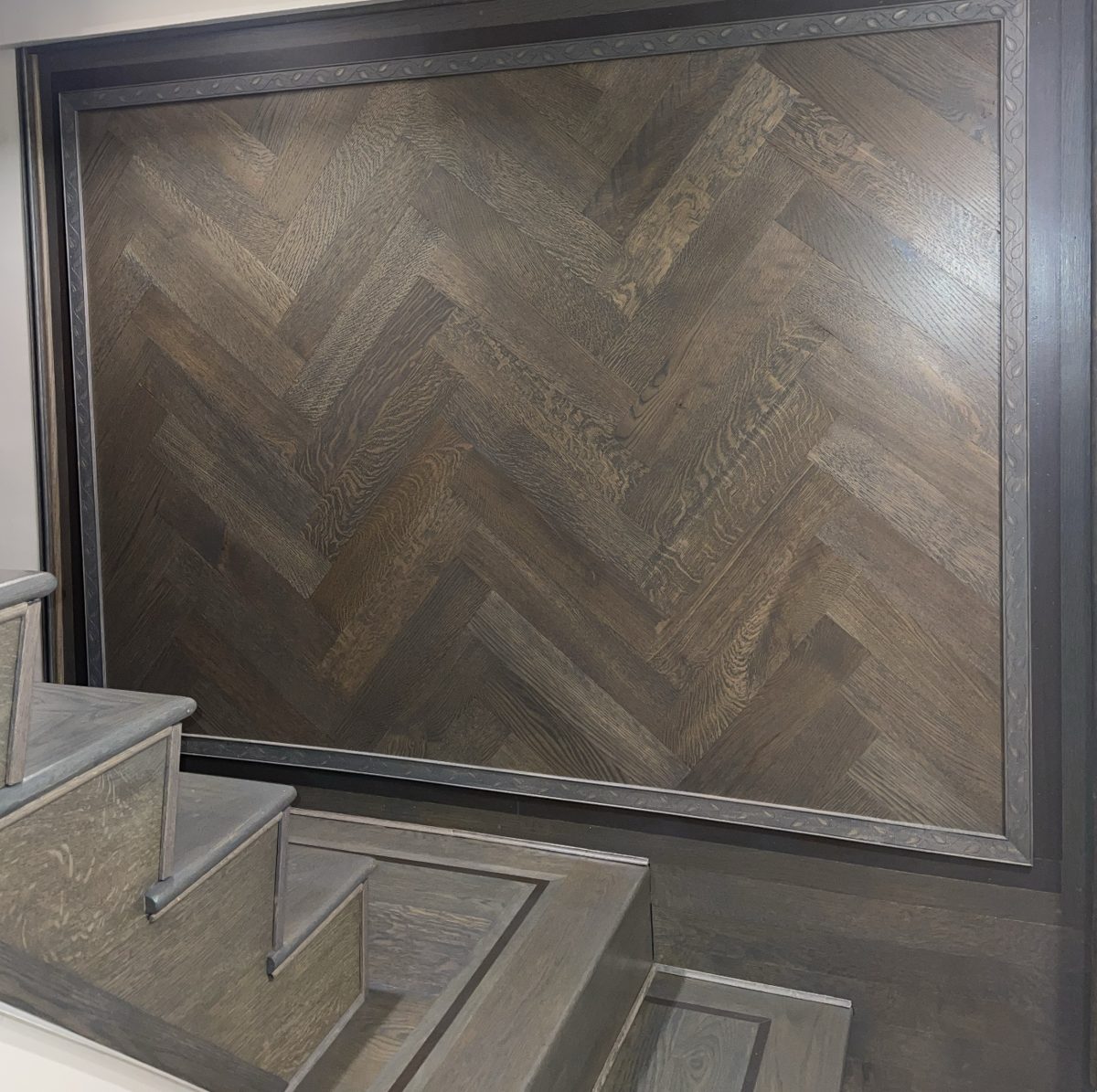 Dark gray-stained herringbone oak wall panel beside matching gray stairs