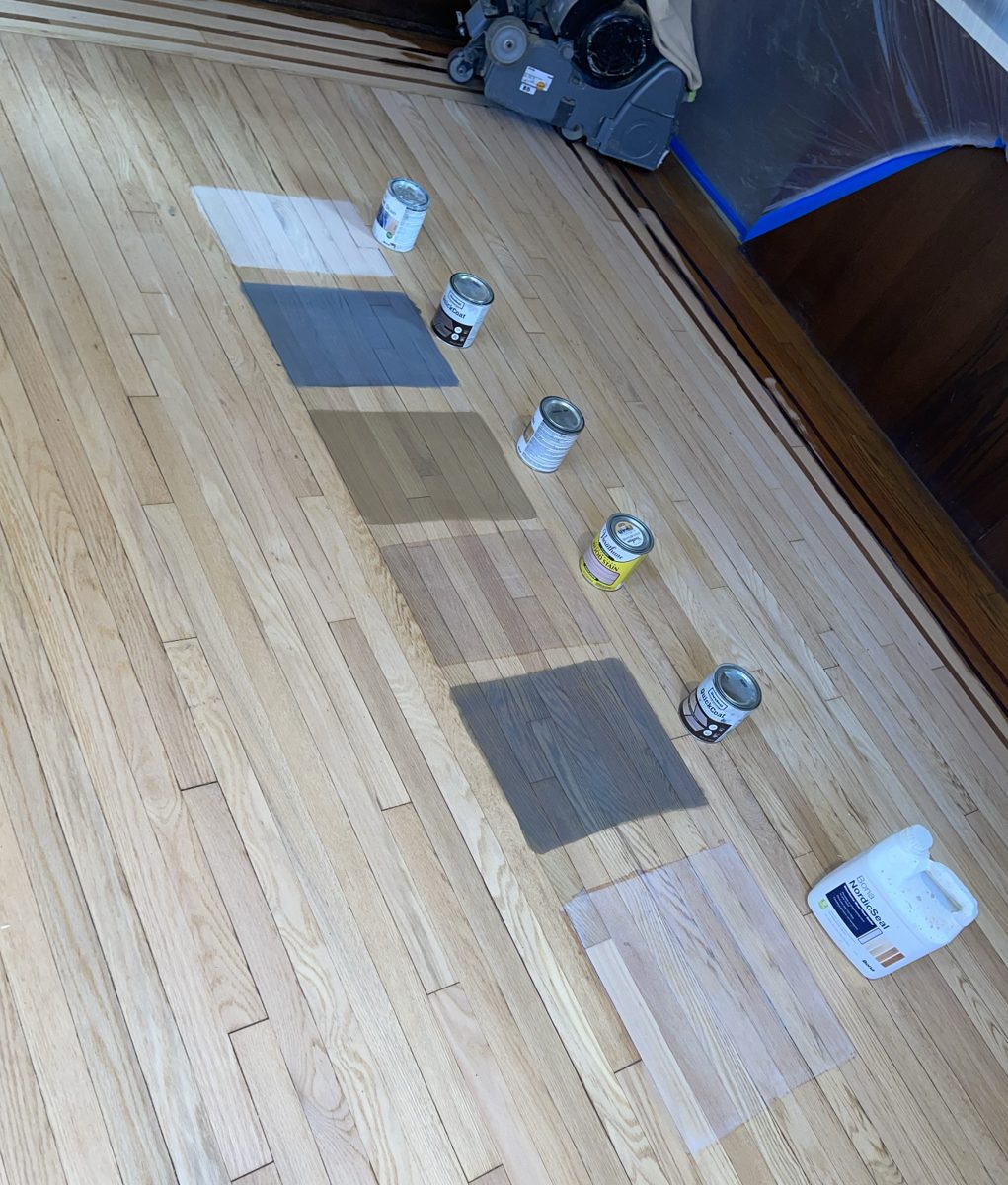 Row of stain color samples on bare oak flooring, with a Bona NordicSeal jug