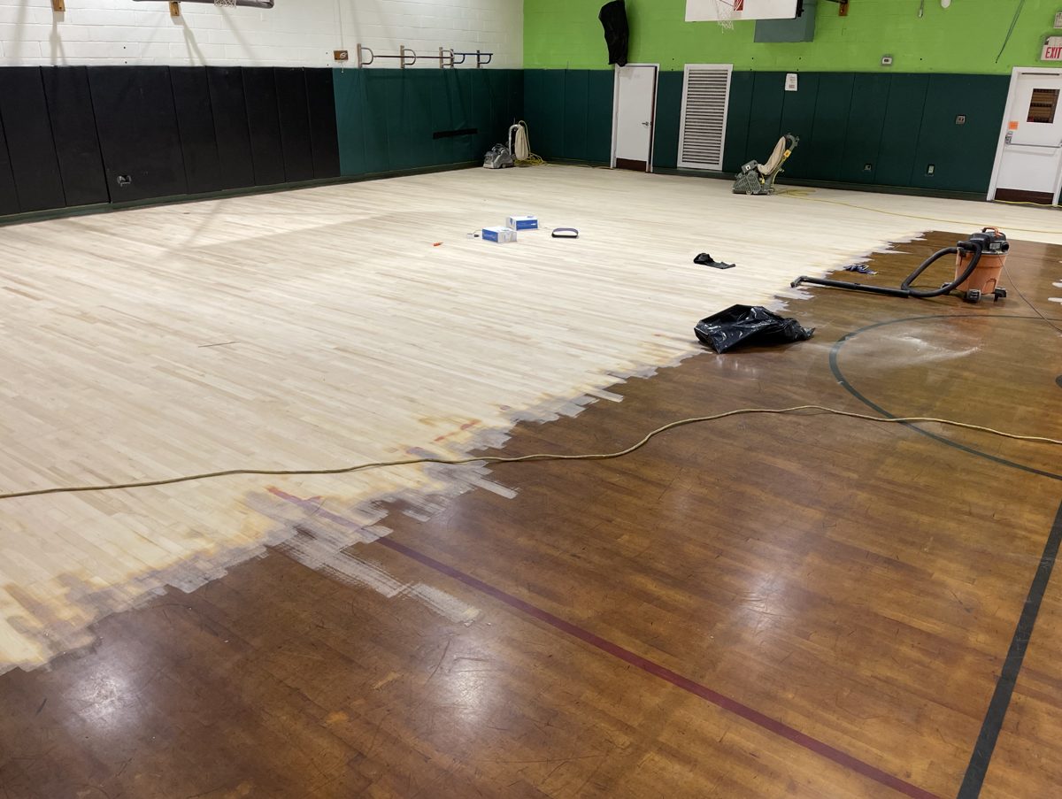 Half of the gym floor sanded to bare wood beside the dark old finish