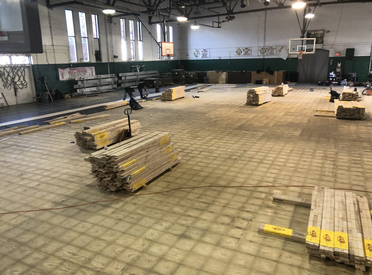 Stacks of hardwood flooring on the exposed subfloor of the gym