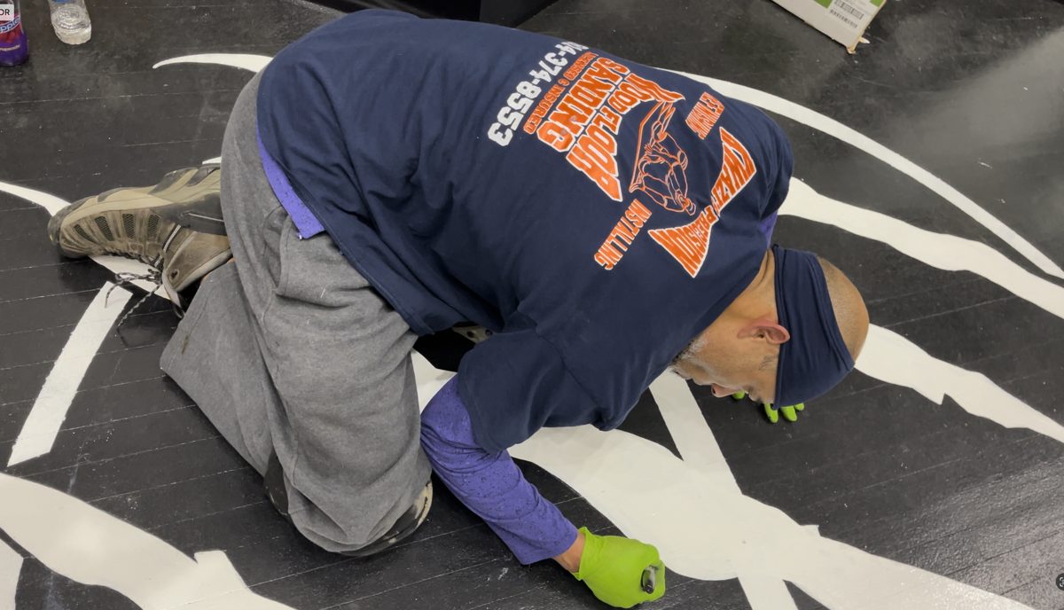 Kwazi painting white logo details on a black hardwood floor