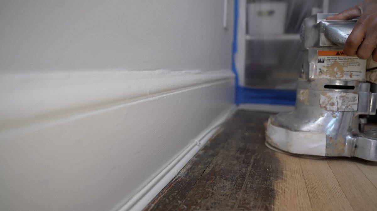 Orbital edge sander working along the baseboard where the old finish is being removed
