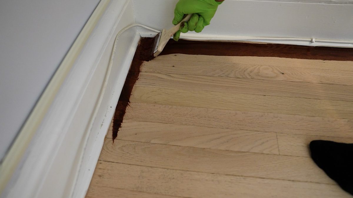 Brushing stain into the corner along the baseboard with a green-gloved hand