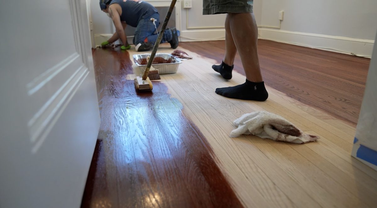 Applying a dark red-brown stain to bare oak flooring with a lambswool applicator